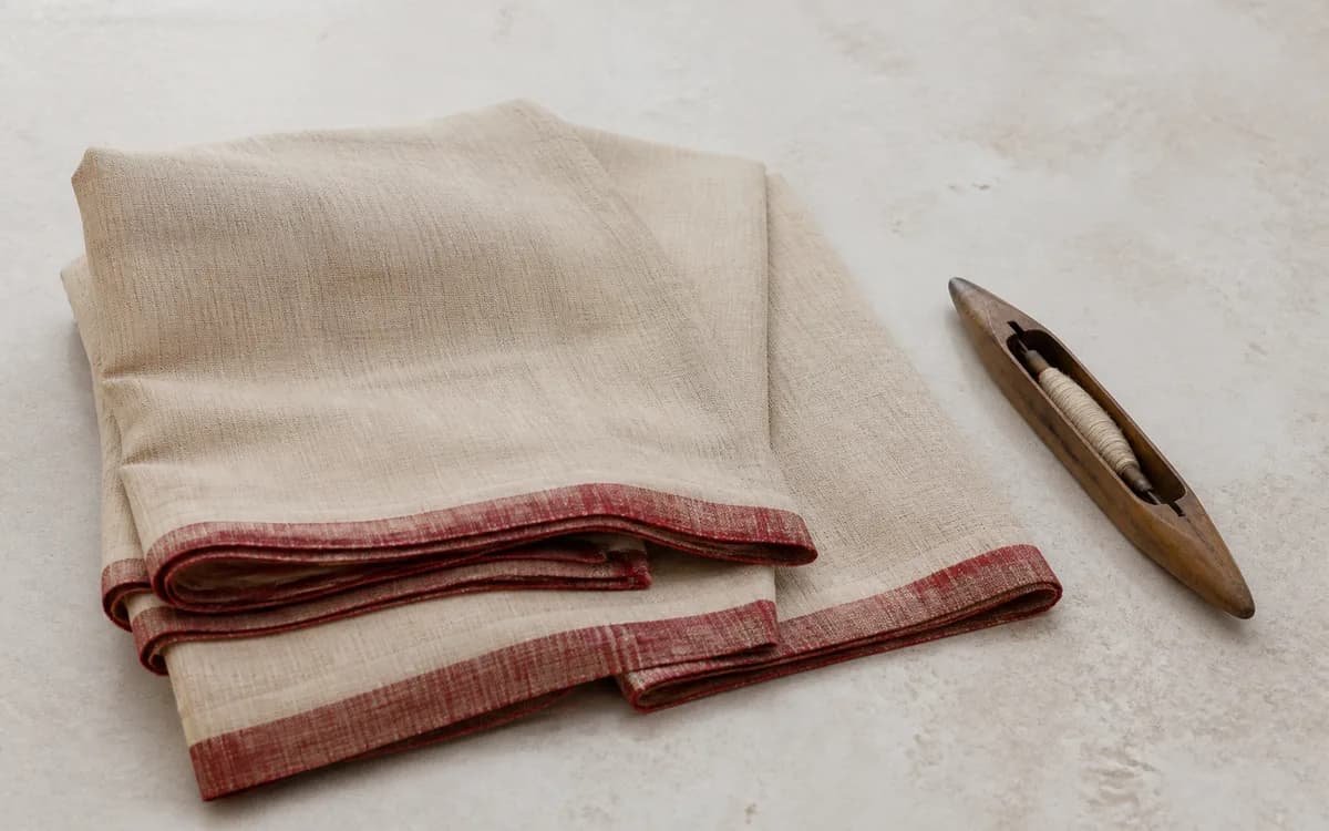Editorial still life of a natural beige handwoven saree with a muted maroon edge, representing sarees sourcing in Surat, Gujarat