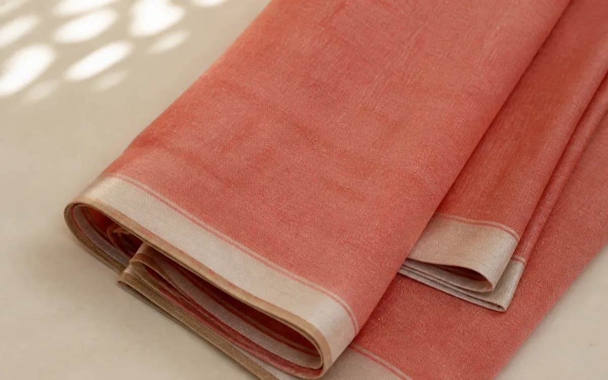 Editorial still life of a folded dusty-coral linen saree, representing sarees sourcing in Surat, Gujarat